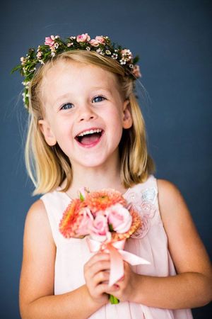 Young child wearing floral crown and pink dress smiles joyfully.