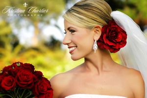 Bride with red rose hair accessory and bouquet smiling against blurred background.