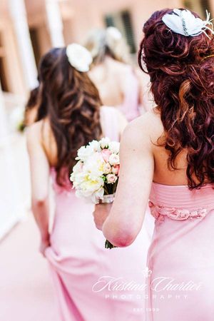 Bridesmaids in pink dresses with curled hair holding white bouquets.