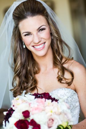 Elegant bride in white dress holding mixed rose bouquet with purple and pink flowers.