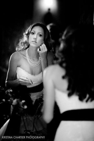 Black and white reflection of bride with pearl necklace applying makeup.