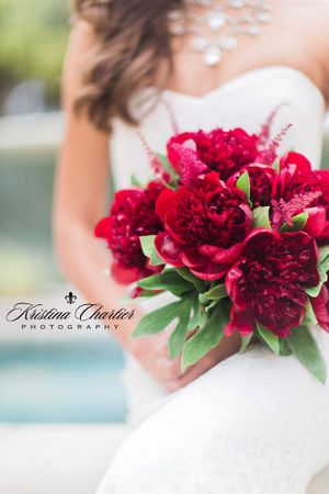 Deep red peony bridal bouquet held against white wedding dress.