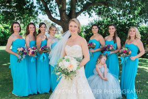 Wedding party in turquoise bridesmaid dresses poses outdoors under tree.