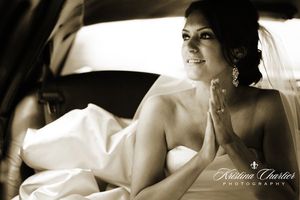 Black and white photo of bride relaxing in vintage car on wedding day.