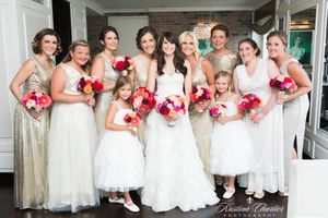 Wedding party in white and cream dresses pose together holding pink bouquets.