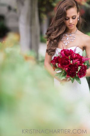 Elegant bride in white dress holding deep red bouquet in garden setting.