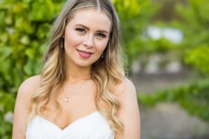 Outdoor bridal portrait featuring a strapless white wedding gown against green foliage.