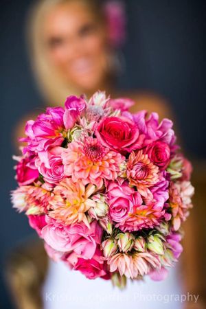 Vibrant pink and coral bridal bouquet with roses and dahlias against dark background.