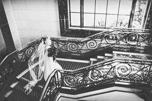 Black and white photo of an elegant staircase with ornate railings and flowing bridal veil.