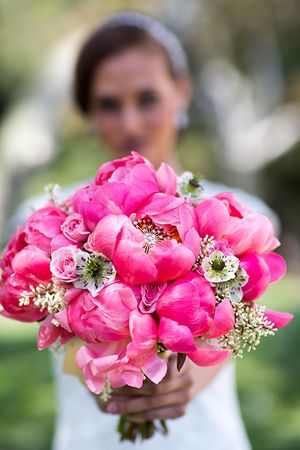 Vibrant pink peony and rose bridal bouquet held against a soft blurred background.