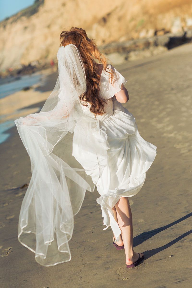 Romantic beach scene with flowing white wedding dress and veil catching the ocean breeze.