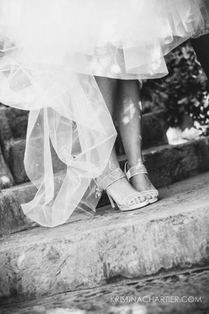 Black and white detail shot of bridal shoes and tulle dress hem on stone steps.