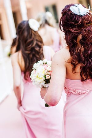 Bridesmaids in pink dresses with burgundy hair holding white bouquets at a wedding ceremony.