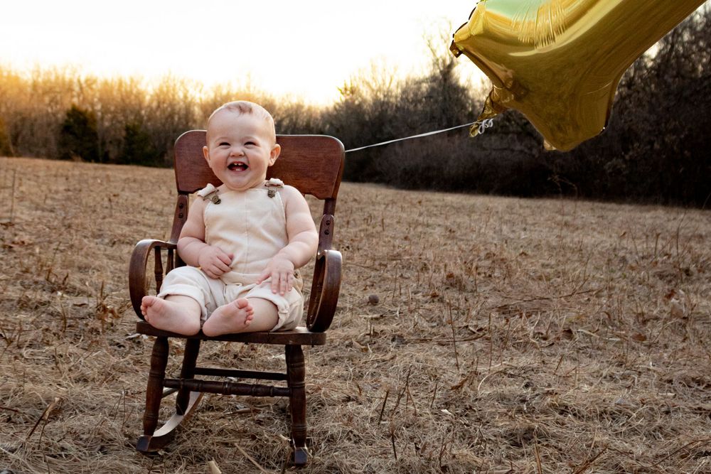baby laughing in rocking chair with number 1 balloon blowing around behind him