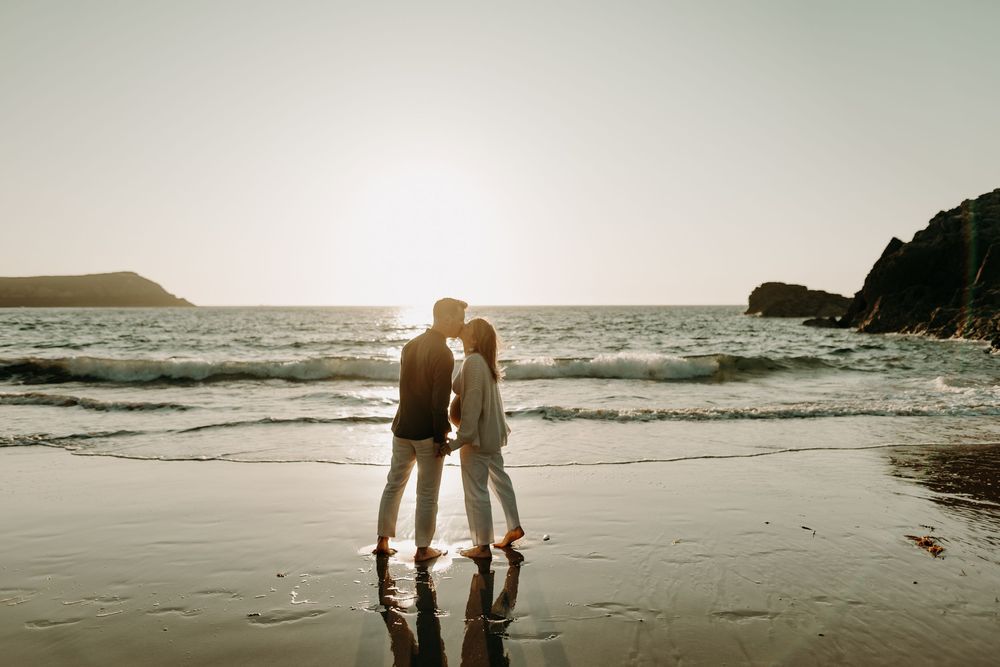 Silhouettes of people walking along a misty beach at sunset with waves crashing in the background.