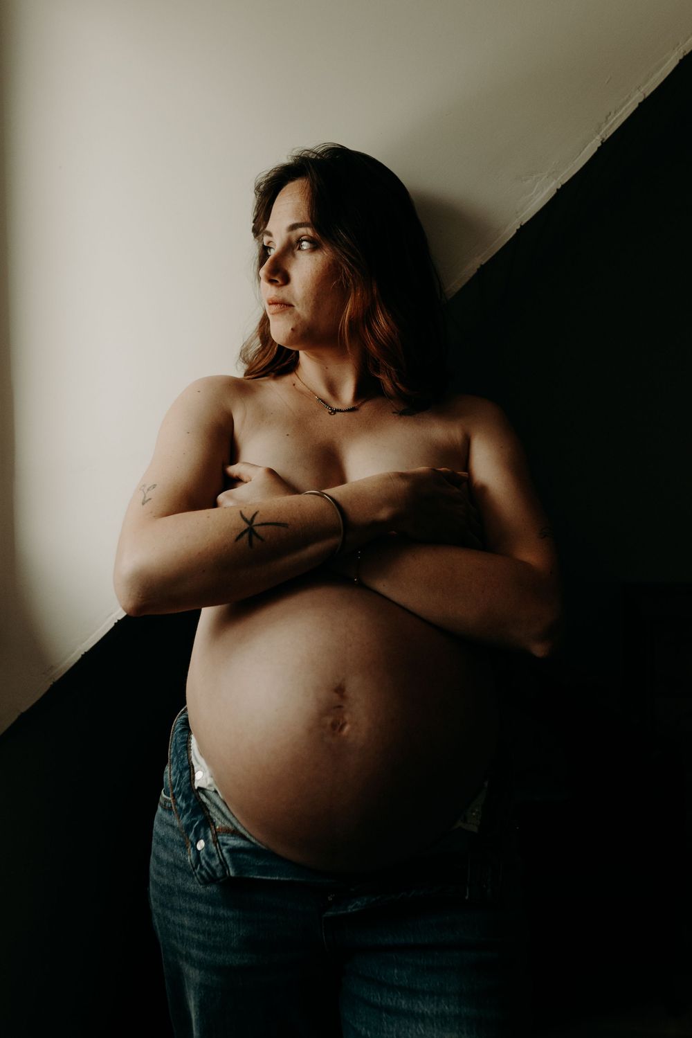 An artistic maternity photo showing a pregnant belly against a dark wall with dramatic lighting and shadows.