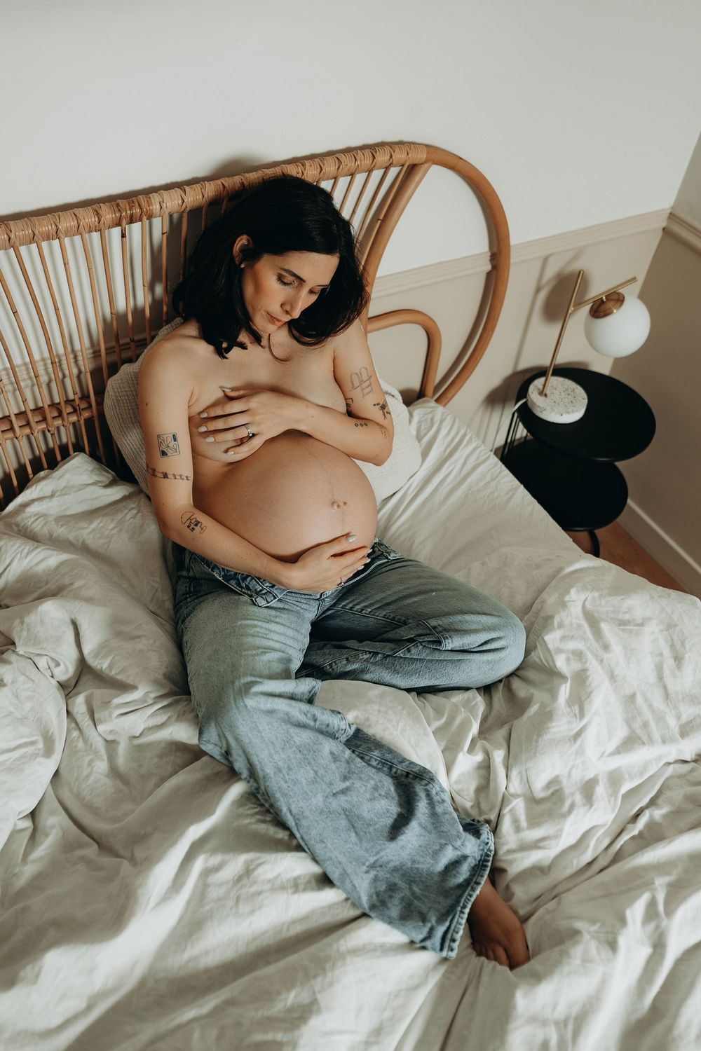 Series of intimate maternity photos showing a pregnant person in jeans resting on white bedding.