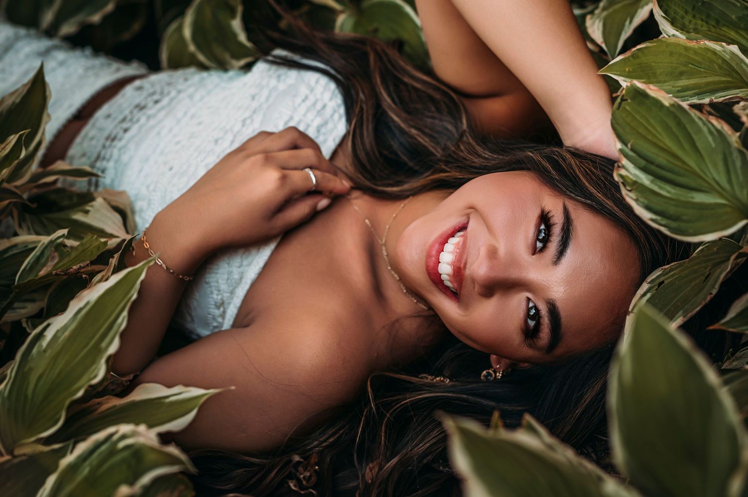 Beautiful smiling woman lying among large tropical leaves for a vibrant outdoor portrait session.
