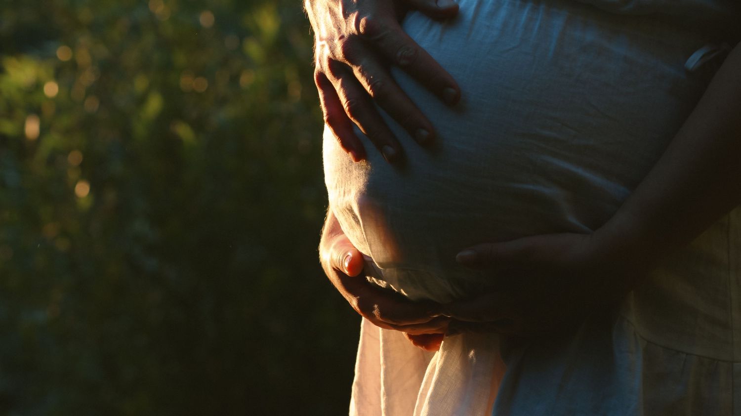 Golden hour maternity photo shoot with the dad's hand touching the belly in the ray of sunlight.
