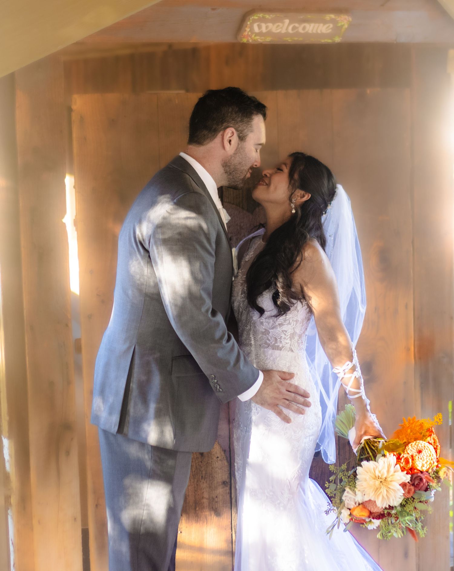 Romantic moment between newlyweds in a sunlit doorway with welcome sign.