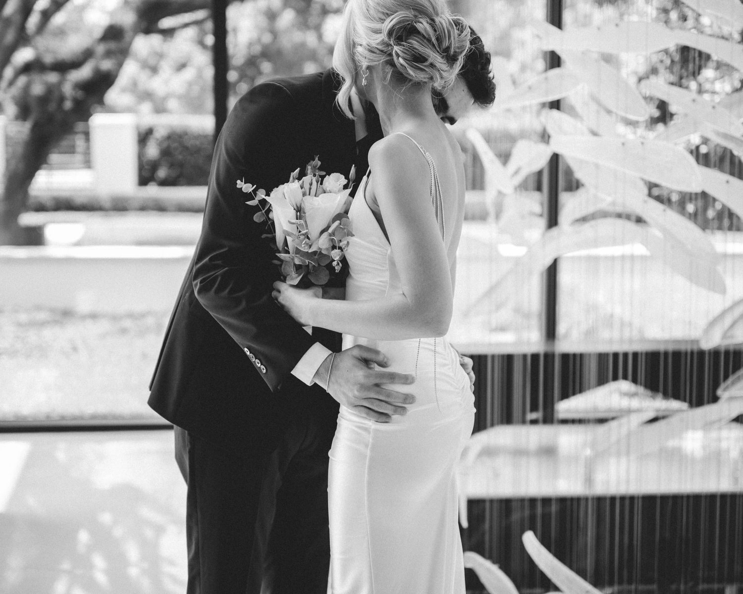 Black and white photo of a bride and groom sharing a romantic kiss at their wedding ceremony.