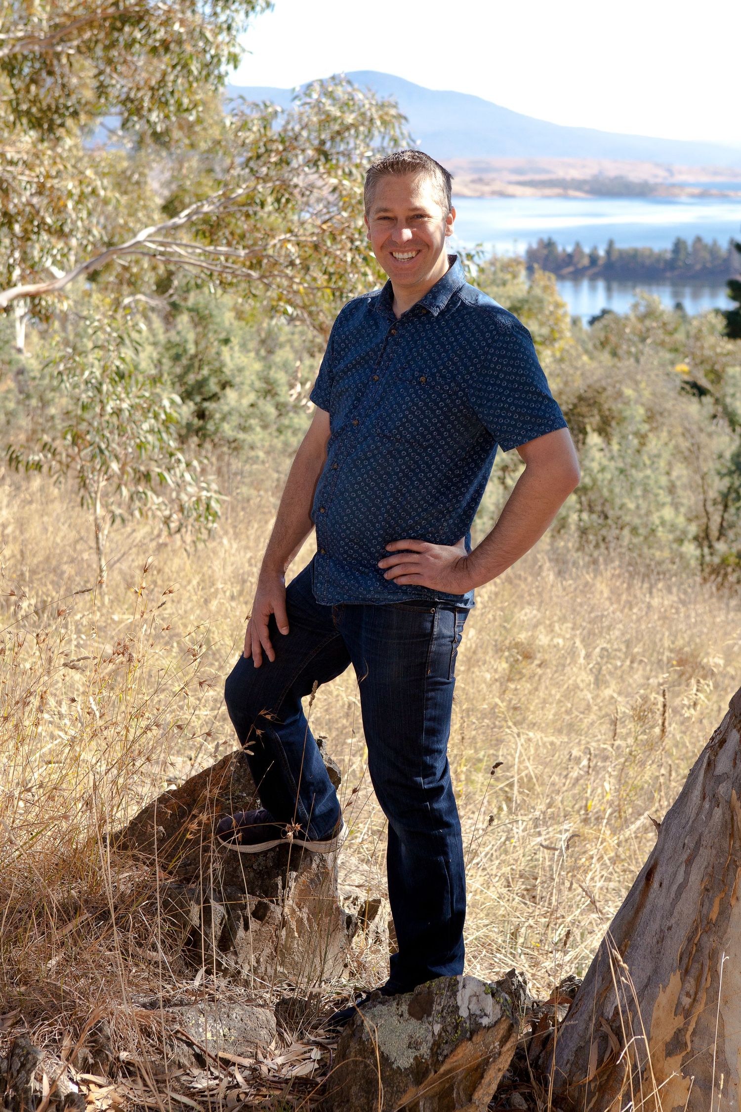 A series of outdoor portrait photos showing someone in a navy polka dot shirt posing near a tree stump with mountains in background.