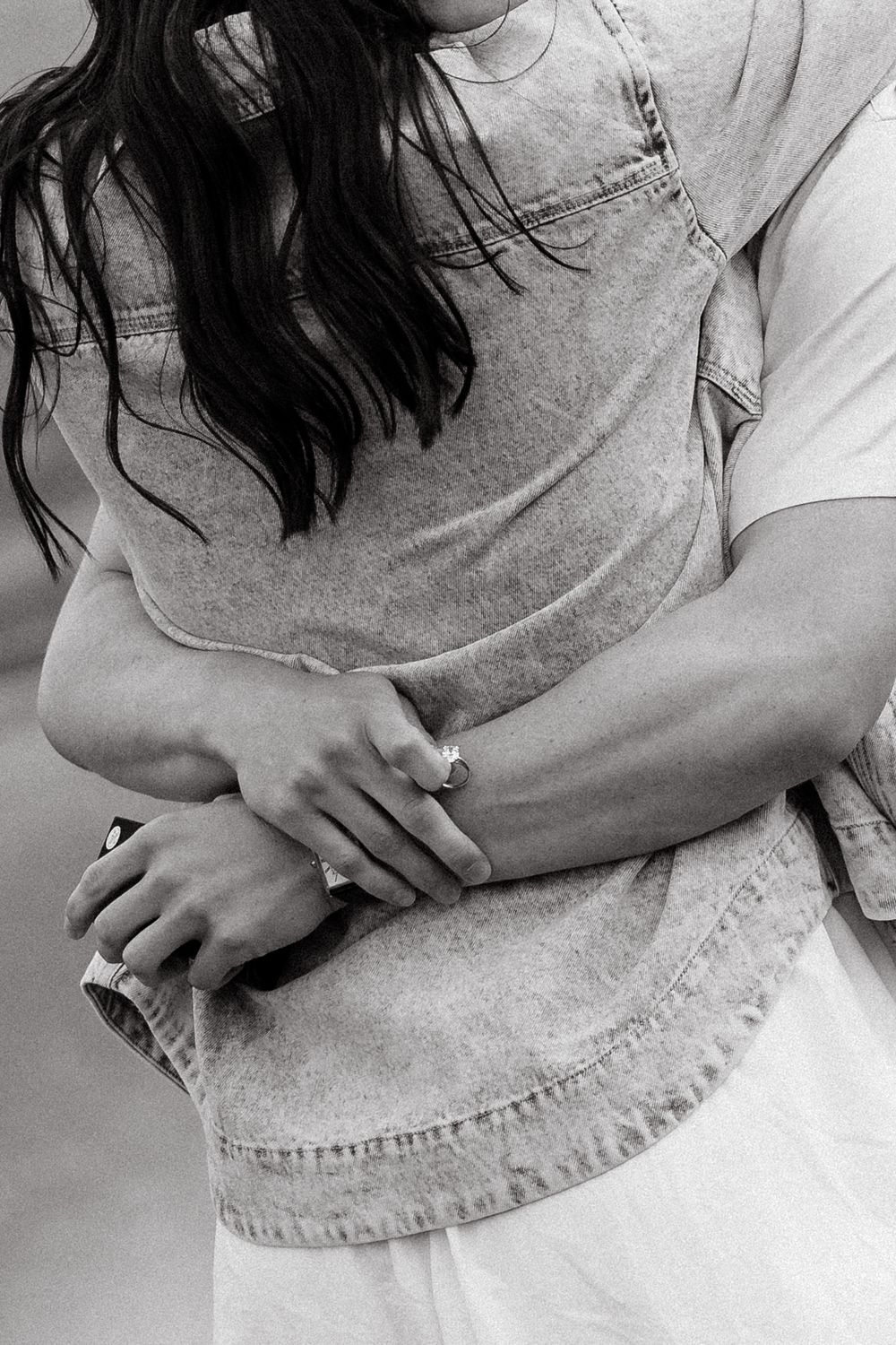 Close-up of hands wearing rings in a tender moment captured in black and white.