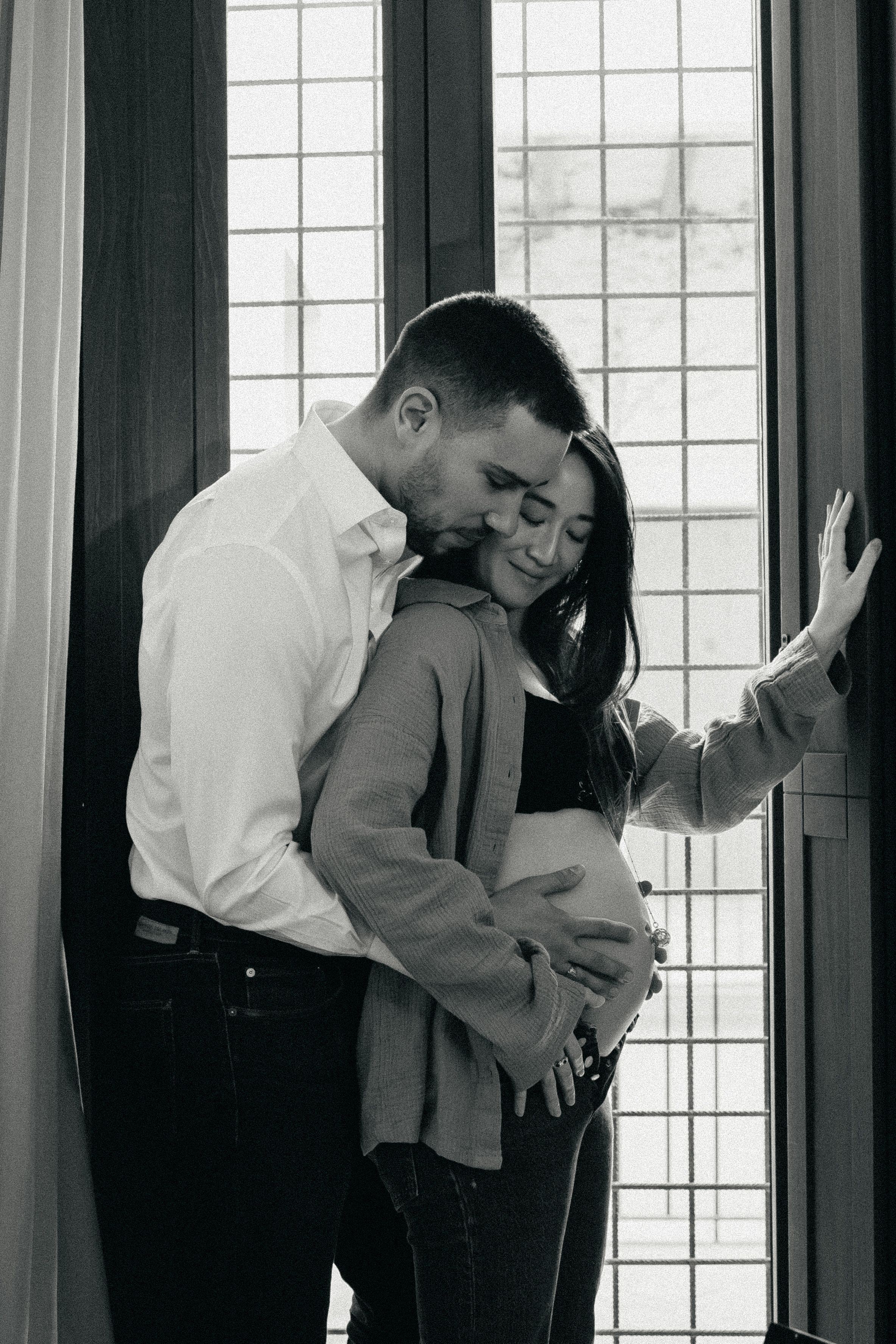 Black and white photo showing dancers in white shirts bending and moving expressively in front of windows.