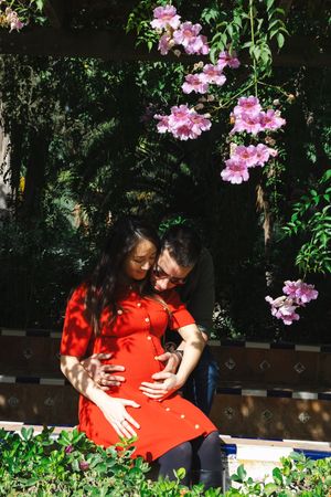A couple embraces tenderly in a garden setting with pink flowers and lush greenery in the background.
