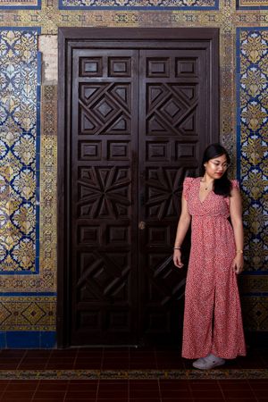 Red floral dress contrasts with dark wooden door and decorative blue tiled wall interior. shooting de femme séville