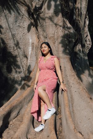 Person in a pink polka dot dress lounges against large tree roots in dappled sunlight.  shooting de femme séville