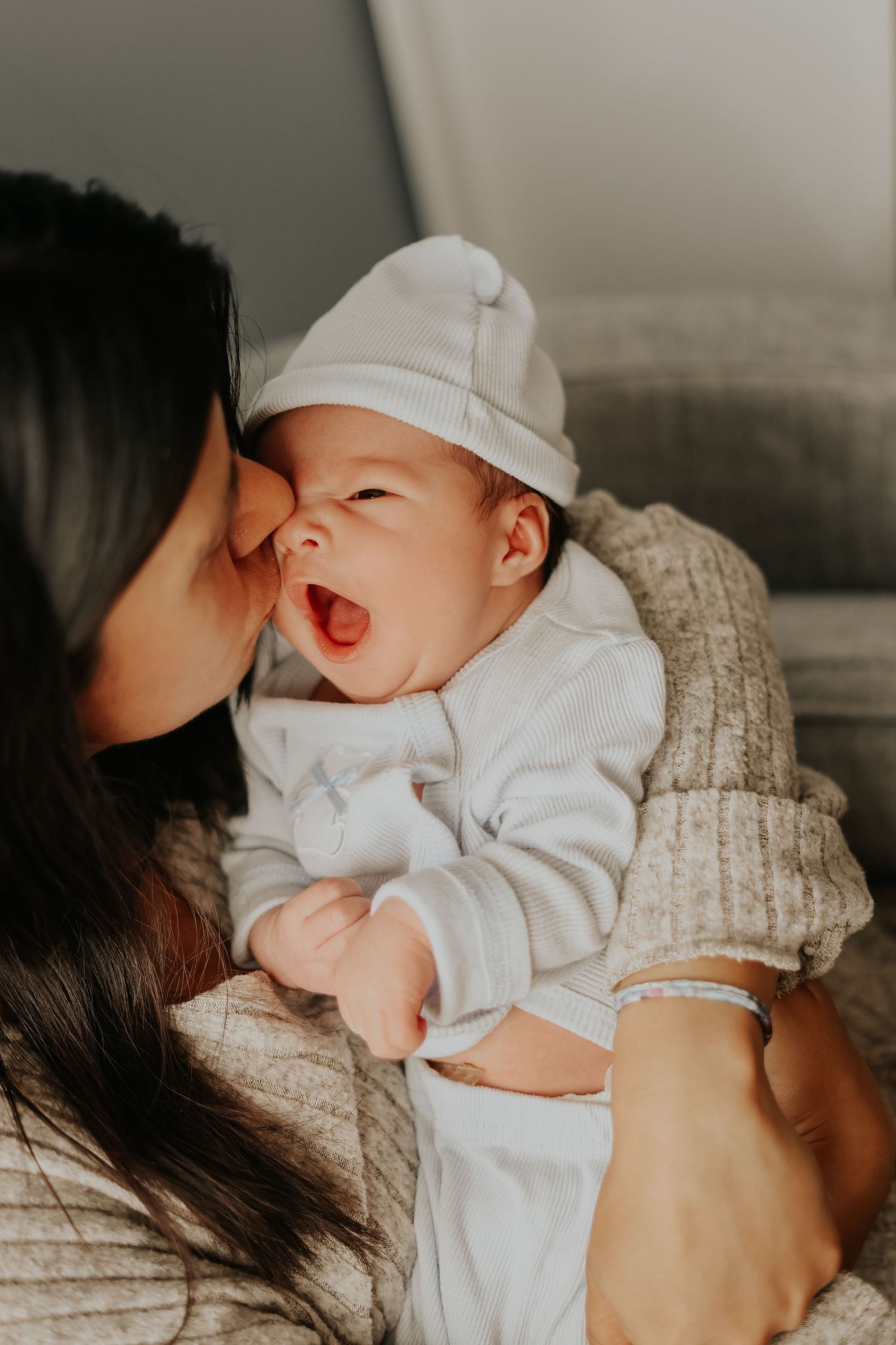 Baby in white hat and outfit smiling while receiving kiss on cheek.