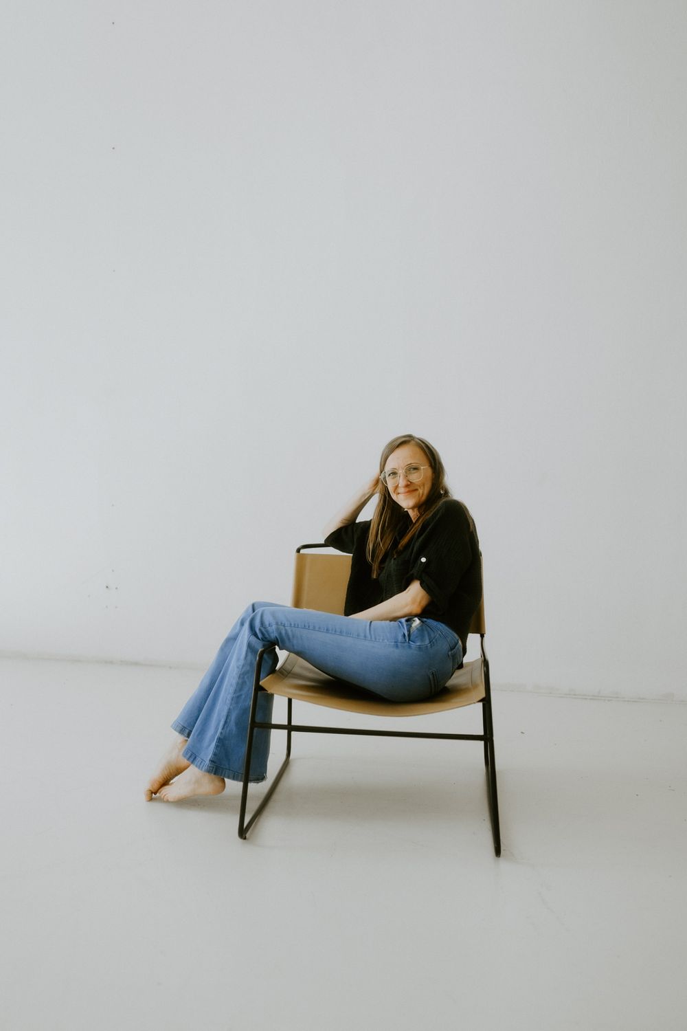 Person in casual attire sits relaxed on a metal chair against white studio background.