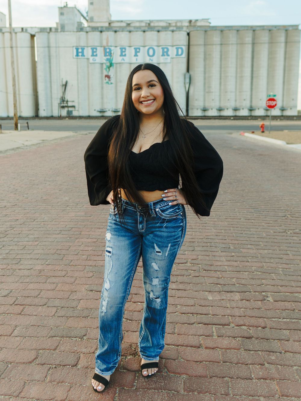 Street style portrait with black crop top and ripped jeans against industrial grain storage facility.
