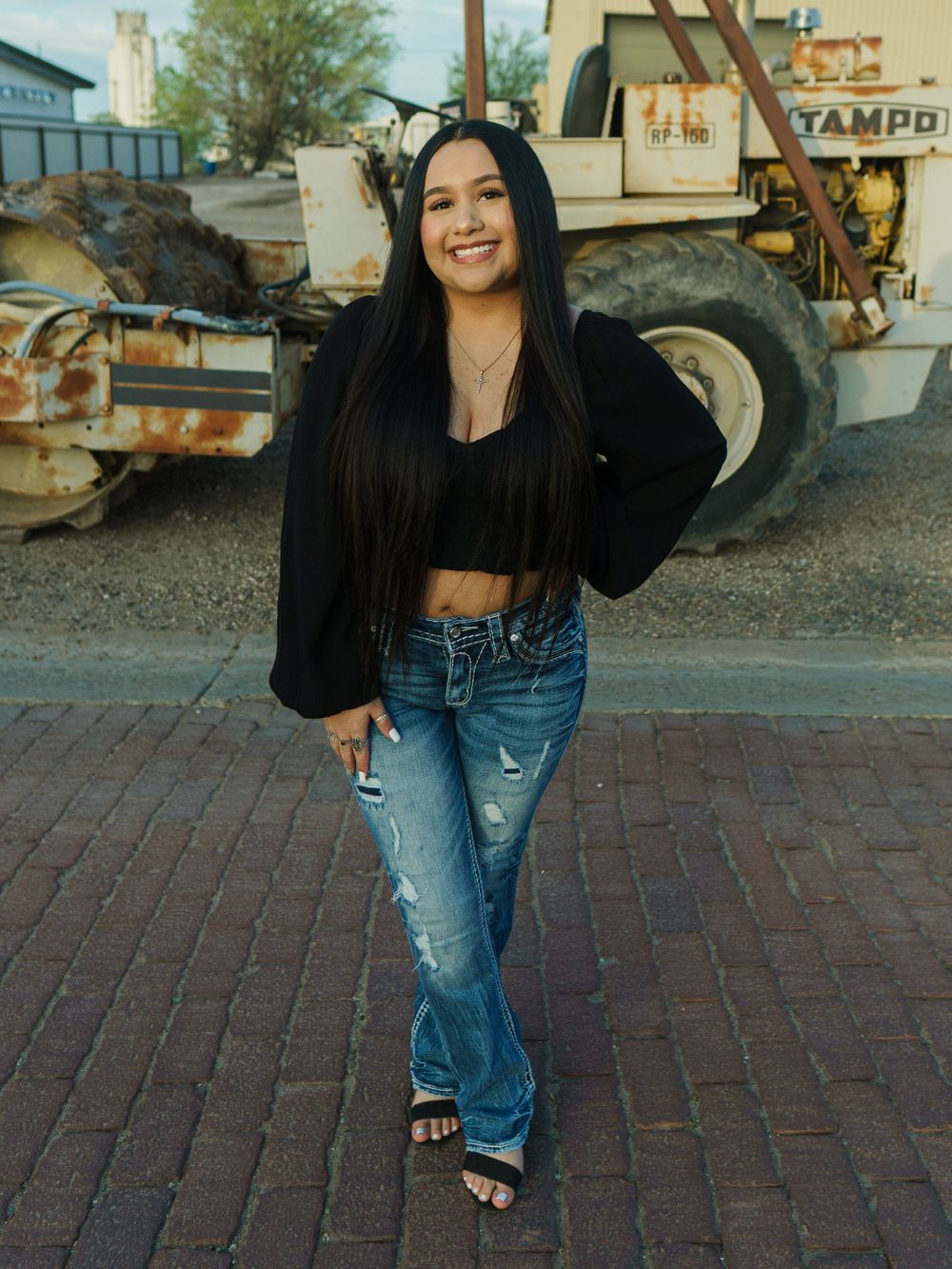 Stylish outdoor portrait with black top and distressed denim against industrial backdrop.