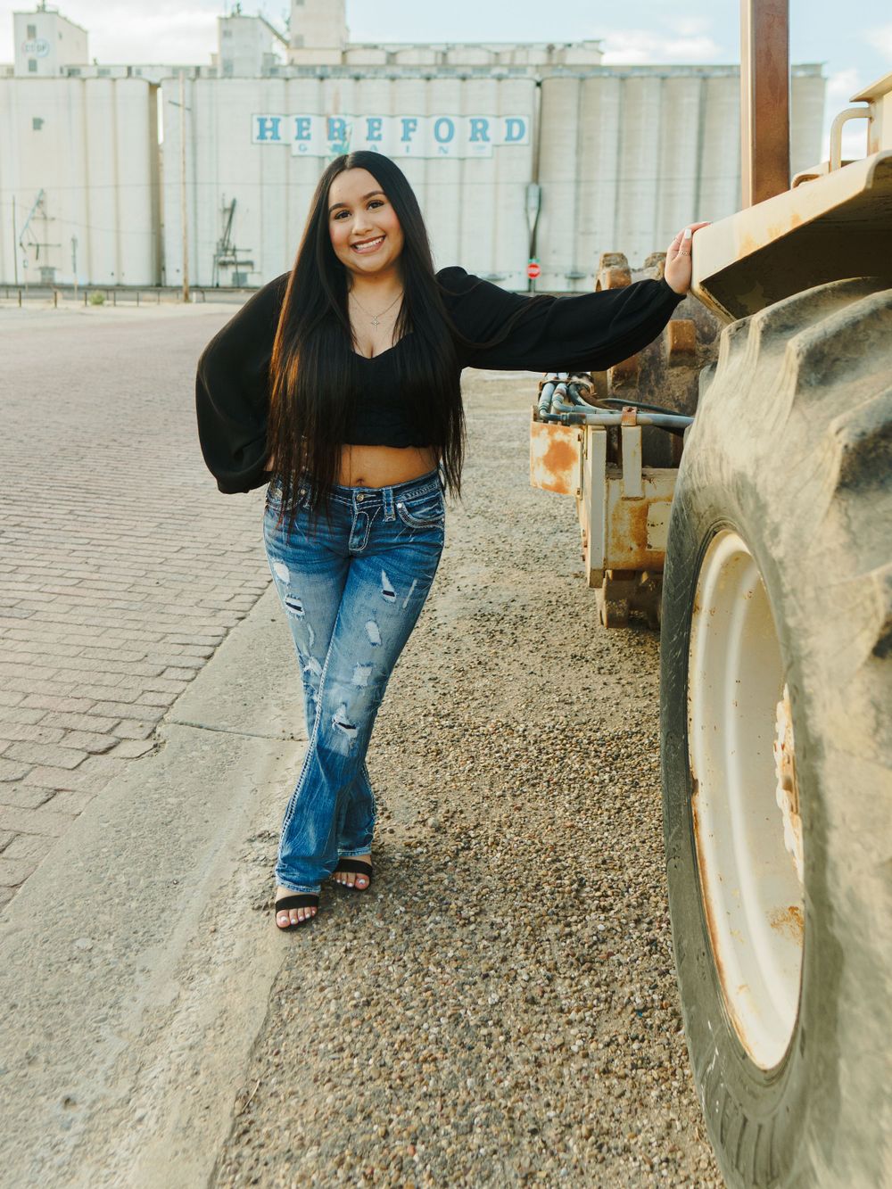 Casual fashion portrait near farm equipment showing trendy crop top and distressed jeans combination.