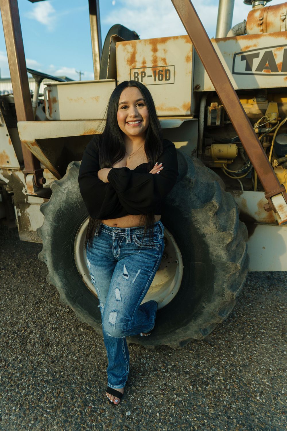 Casual fashion portrait against vintage tractor tire showing modern crop top and jeans combination.