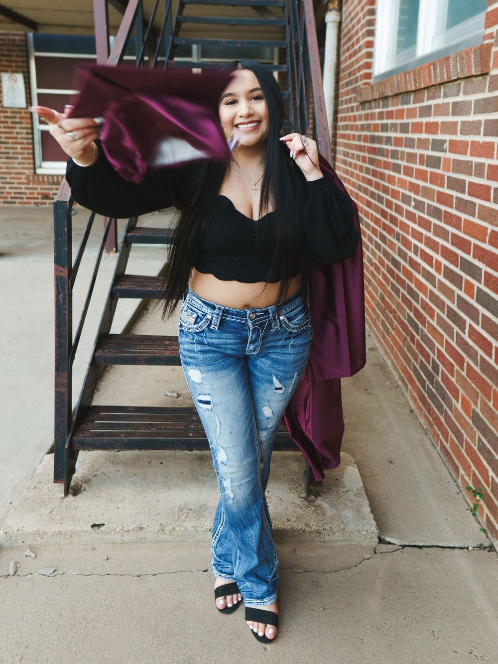 Urban style portrait on brick stairway featuring black crop top and distressed denim outfit.
