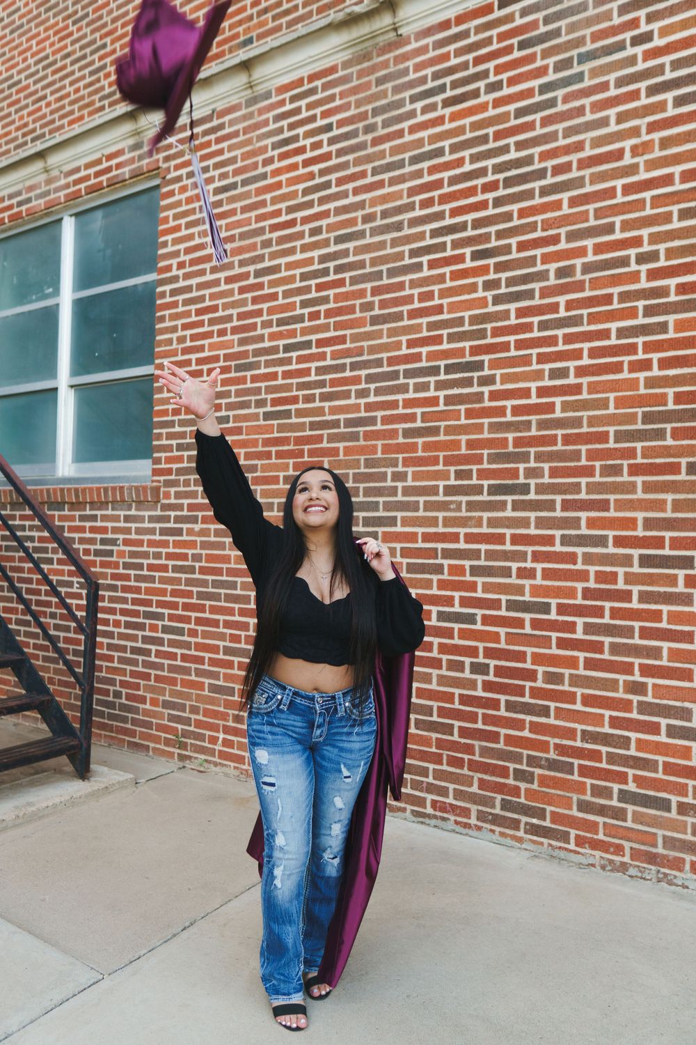 Graduate tosses maroon cap in celebration by brick building.