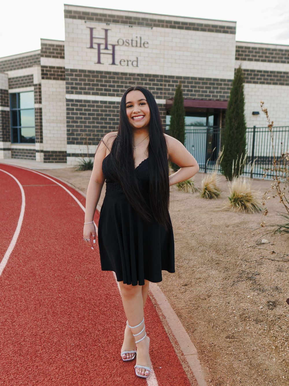 Woman in black dress poses on red track outside Hostile Herd building.