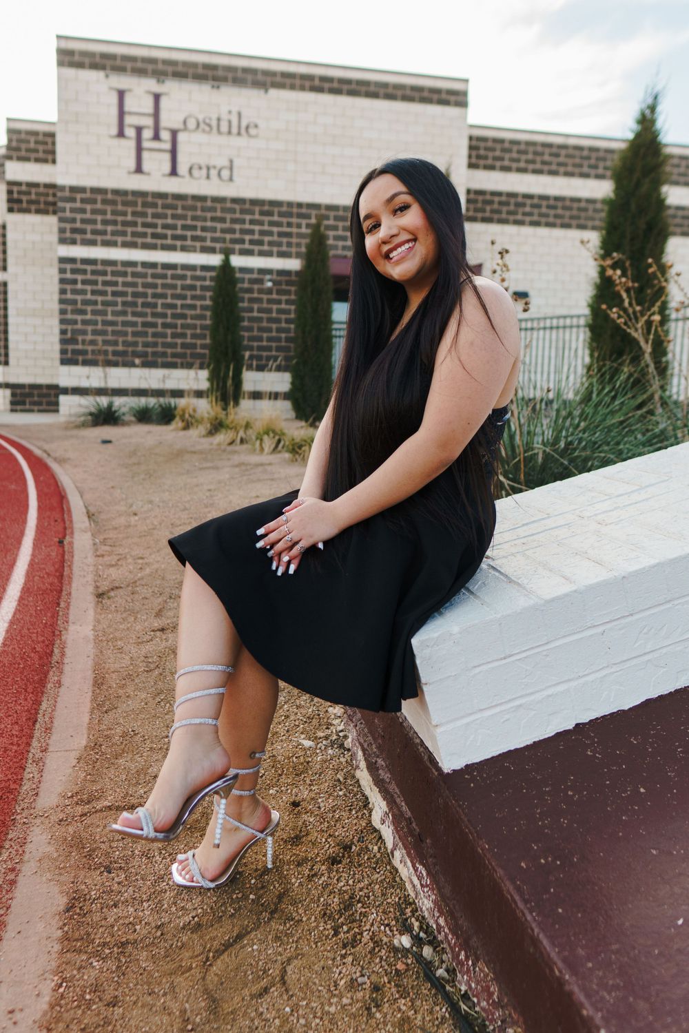 Woman in black dress sits on wall near athletic track.