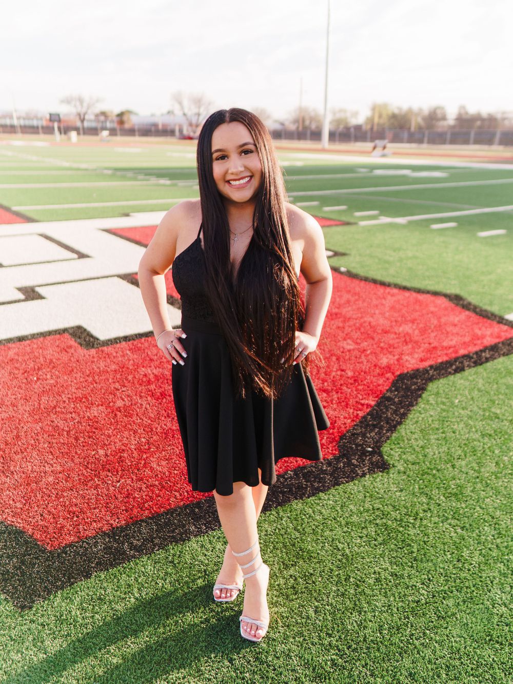 Woman in black dress poses on athletic field with red and green turf.