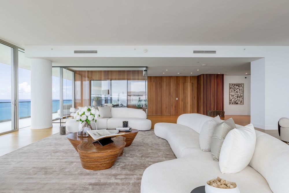 Luxurious open-plan living area with white furnishings and wooden accents overlooking the ocean.