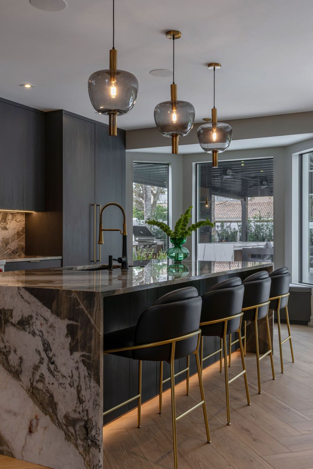 Modern kitchen bar with black leather stools, marble countertops, and elegant pendant lighting fixtures.