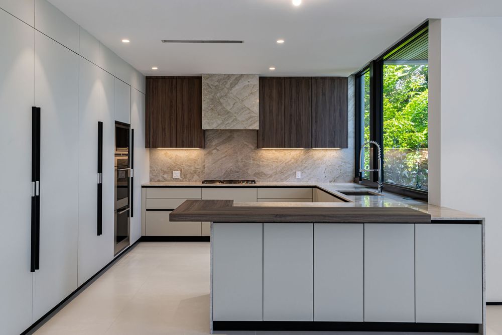 Contemporary white kitchen with dark wood accents and large windows bringing in natural light.