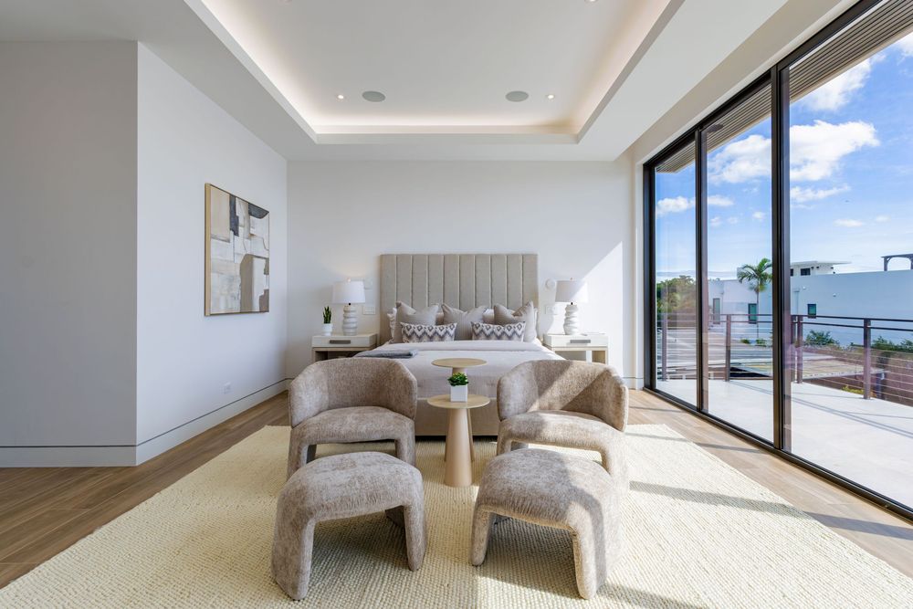 Bright penthouse bedroom with panoramic windows and modern white furnishings overlooking city views.