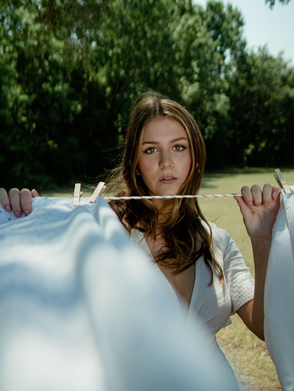 Artistic portrait through laundry line with white sheets creating dreamy outdoor atmosphere.