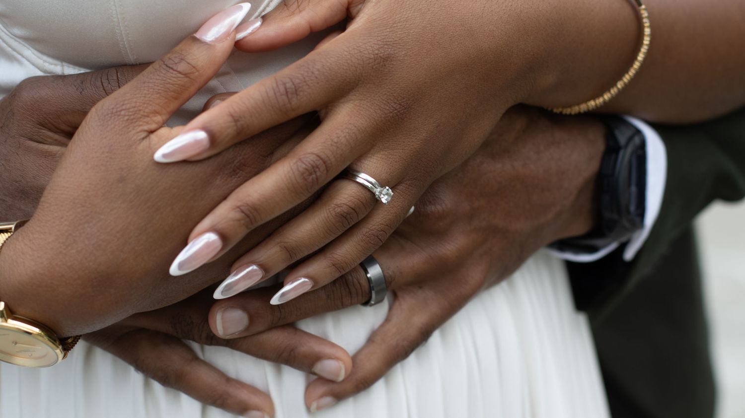 Close-up of hands with wedding rings showing manicured nails and jewelry.