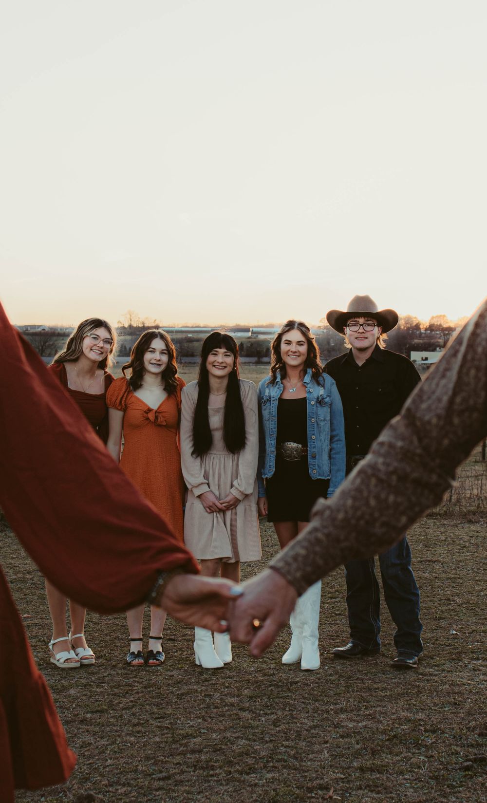 Group photo of people standing together at sunset in a rural field with hands in foreground.
