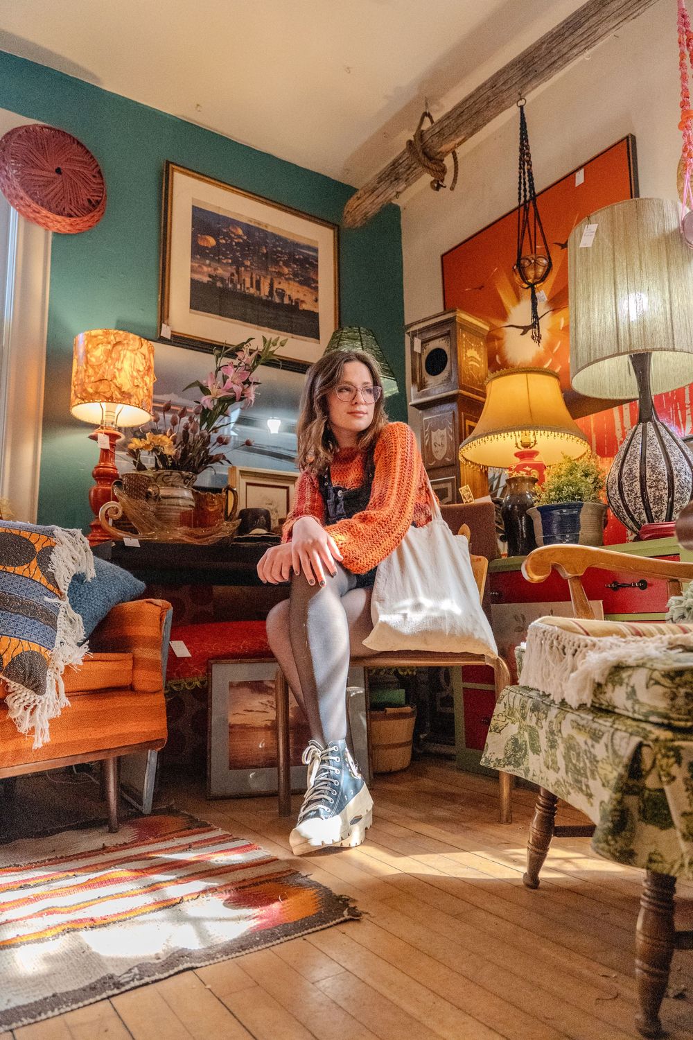 Eclectic vintage room with orange and teal walls decorated with retro lamps, furniture and decor in warm sunlight.